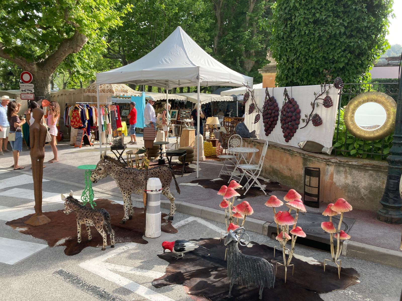 Stand Antic House au marché de Saint-Tropez : sculptures d'animaux, champignons décoratifs et miroir doré